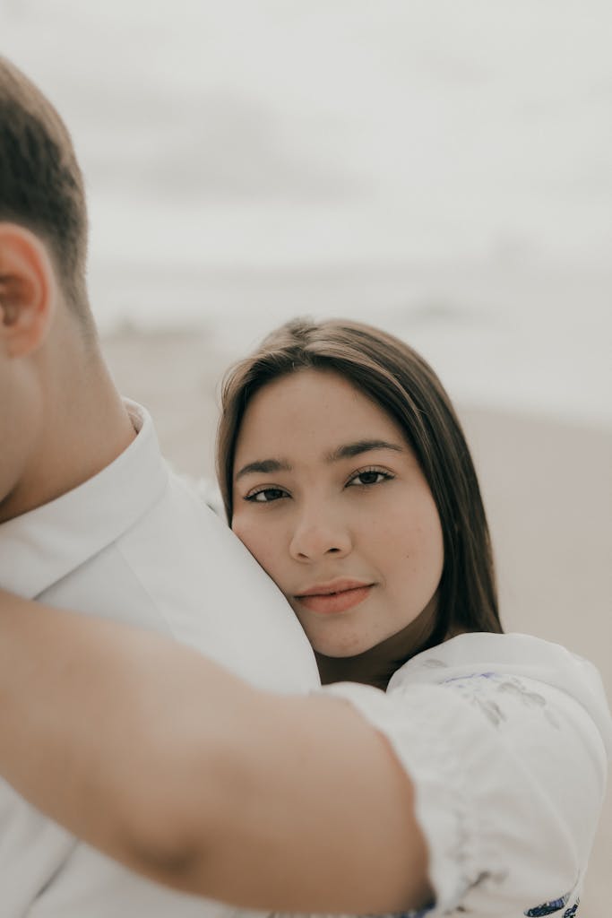 A young woman embraces a man gently on a serene beach, exuding warmth and connection.