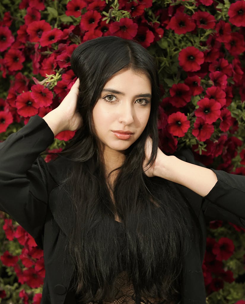 A young woman in black poses gracefully against a backdrop of vibrant red petunias.