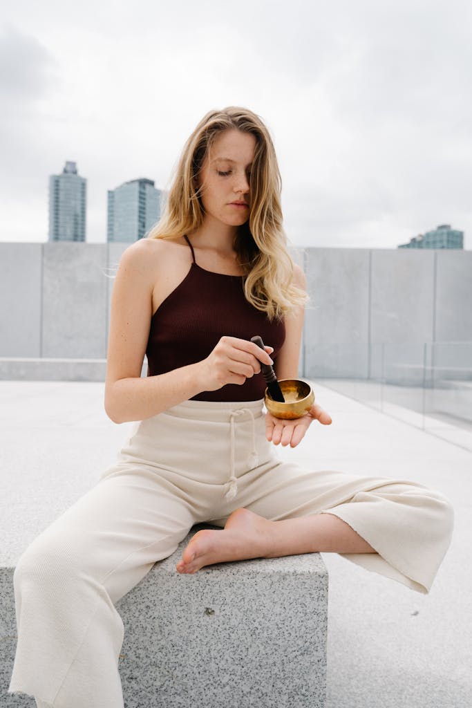 A young woman sitting outdoors using a singing bowl, promoting relaxation and mindfulness.