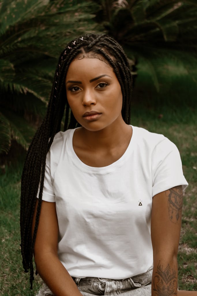 A young woman with braided hair sits outdoors, exuding a serious and pensive look.