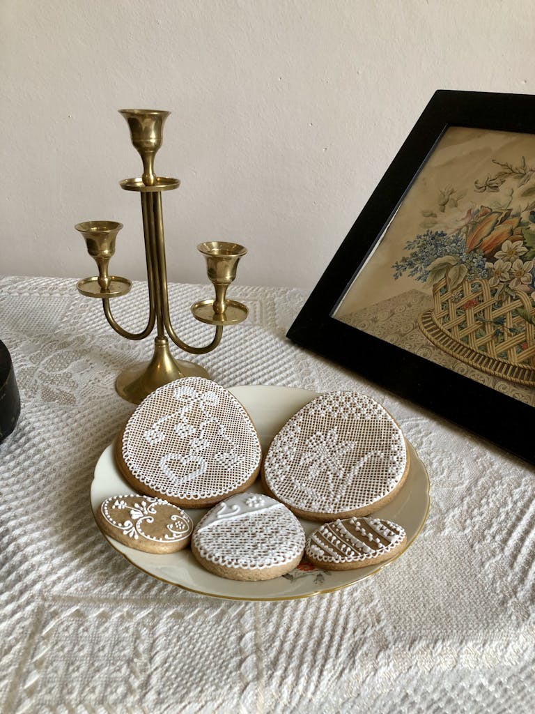 Artistic display of lace-patterned cookies with a brass candle holder and vintage artwork.