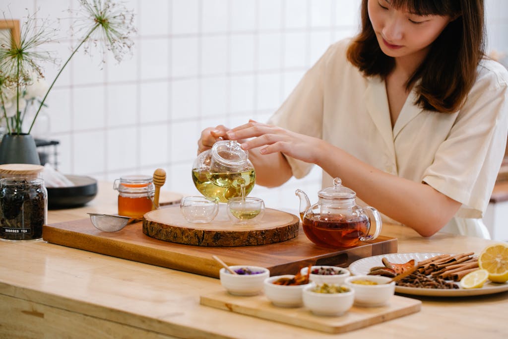 Asian woman pouring tea in a cozy kitchen setting with herbs and spices.