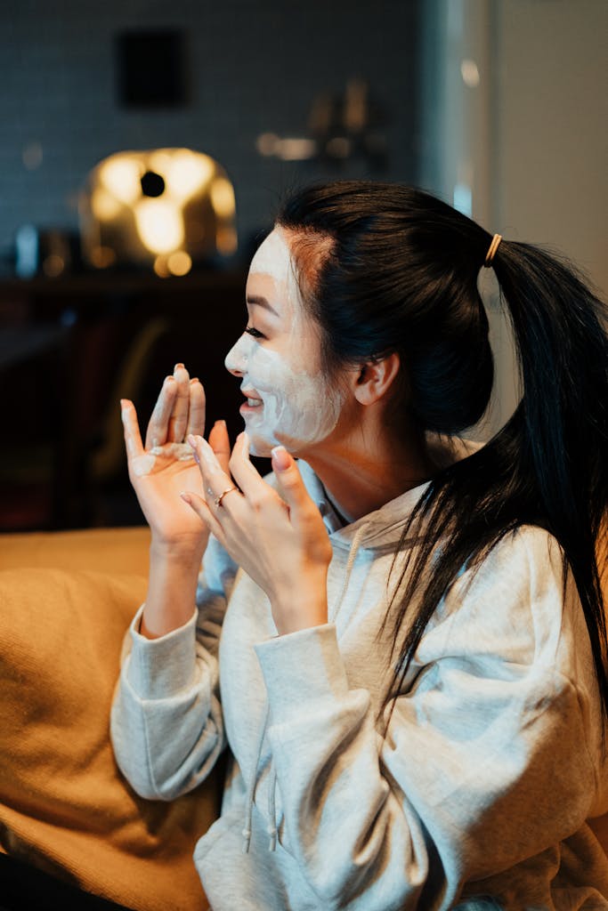 Asian woman relaxing at home with a skincare face mask, enjoying a self-care ritual on a cozy evening.