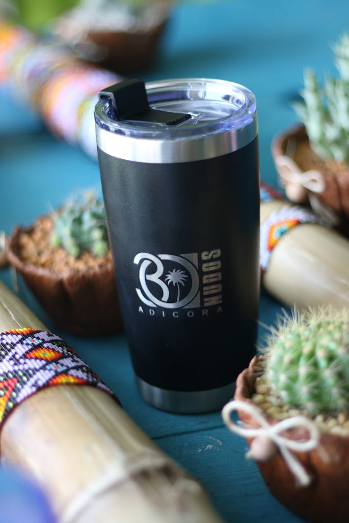 Black travel mug surrounded by Cacti and vibrant decorations on a teal surface.