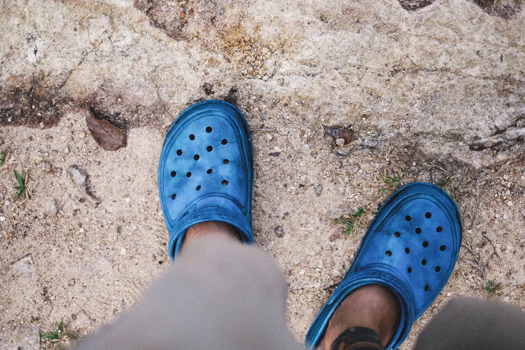 Blue rubber clogs on sand, highlighting relaxed outdoor style.