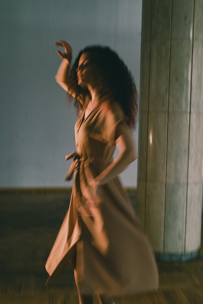 Blurred motion image of a woman dancing gracefully indoors, in soft lighting.