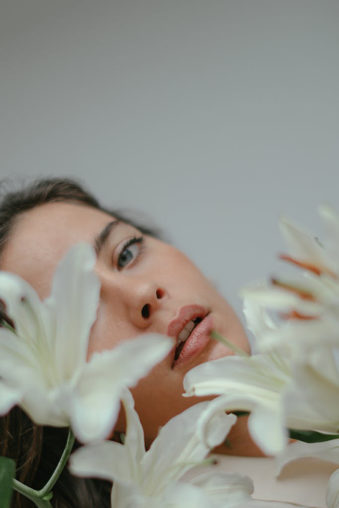 Captivating close-up portrait of a woman surrounded by white lilies, exuding serenity and elegance.