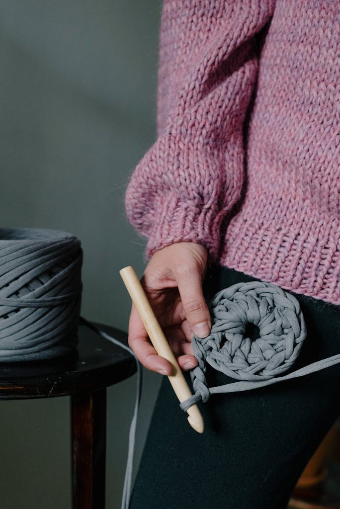 Close-up of a woman crocheting with grey yarn and a wooden hook, showcasing handmade craft for leisure or hobby.