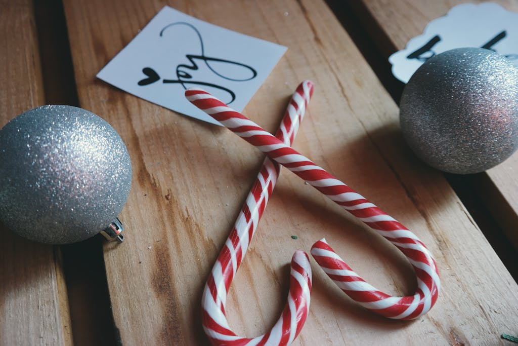 Close-up of candy canes and silver Christmas balls on wooden surface, evoking holiday spirit.