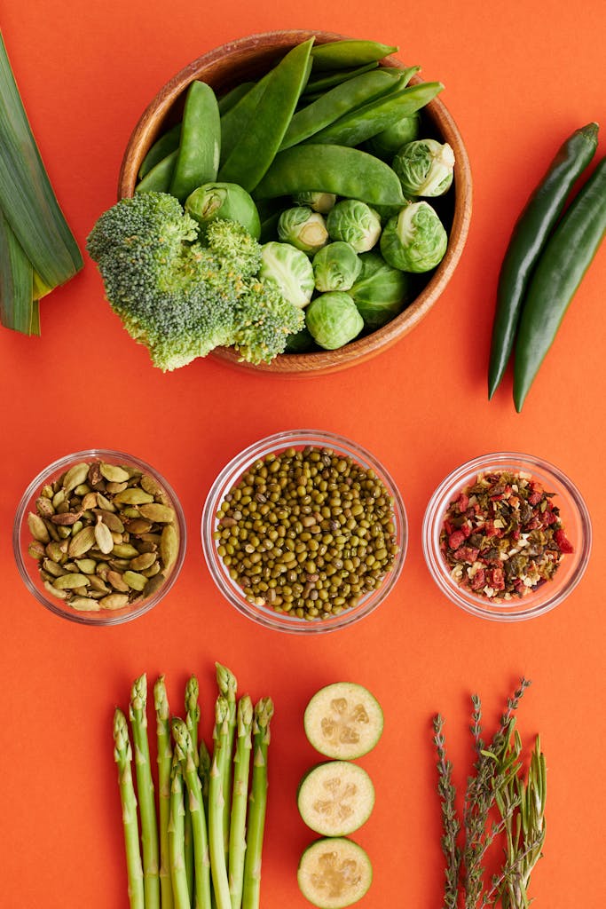 Colorful array of vegetables and spices on an orange backdrop, featuring beans and greens.