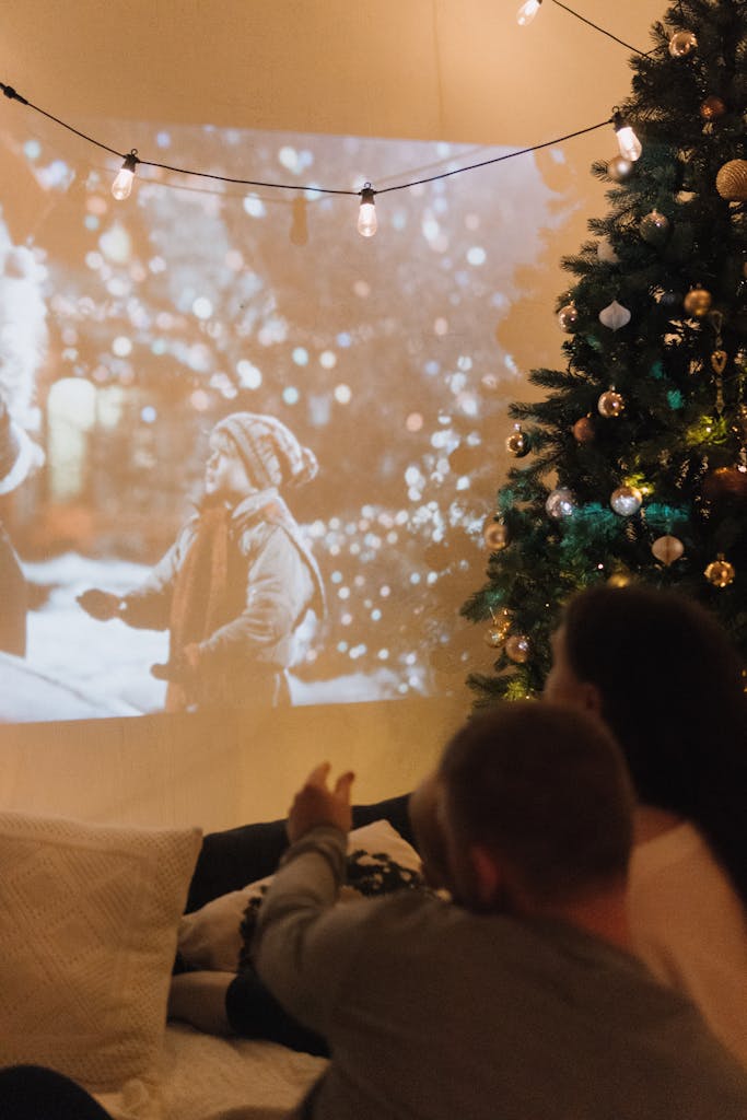 Couple enjoying a festive movie night with a Christmas tree and projector indoors.