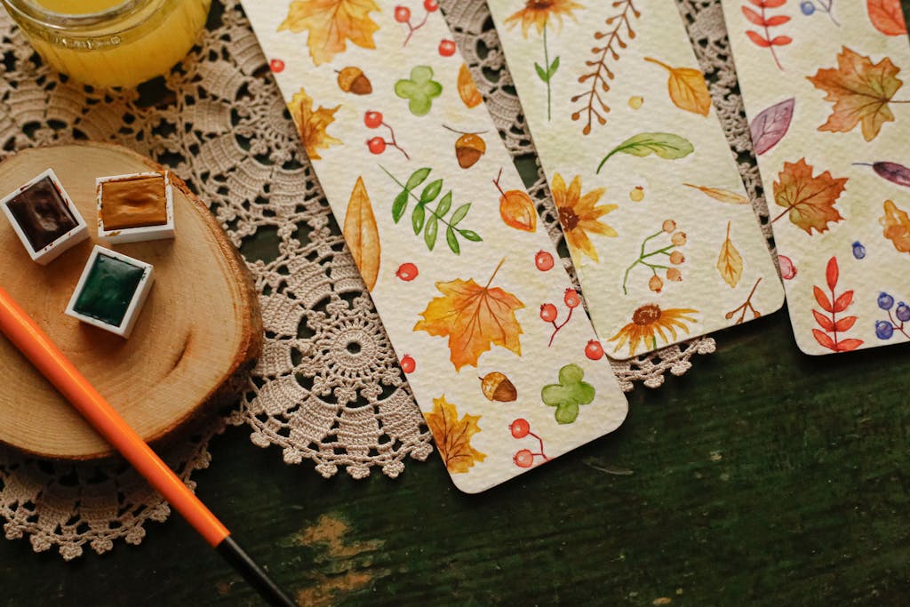 Elegant autumn-themed watercolor bookmarks with leaf patterns and paint supplies on a rustic table.