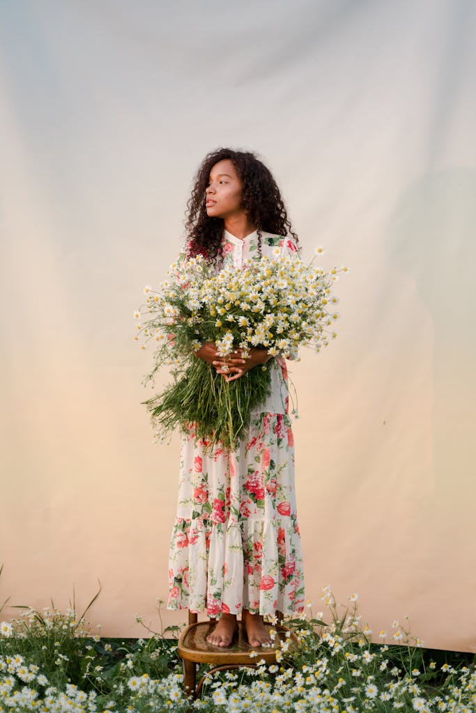 Elegant woman in a floral dress holding a chamomile bouquet, standing on a stool.