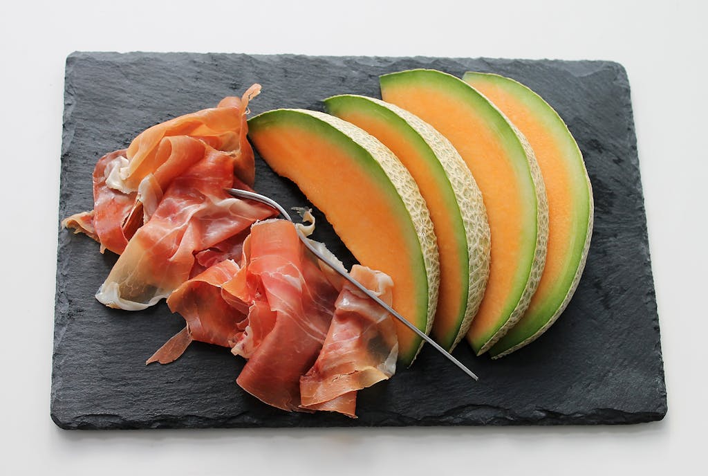 Freshly sliced melon with ham on a slate board, ideal for gourmet food concepts.