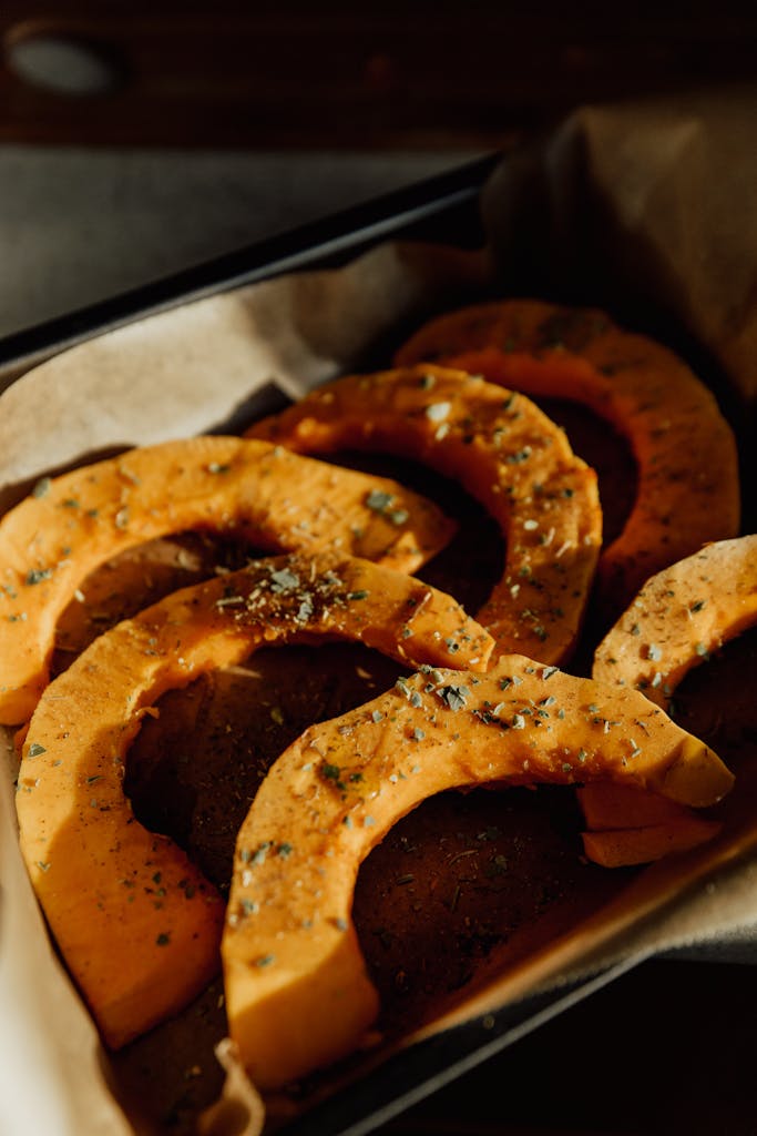 Golden roasted pumpkin slices seasoned with herbs in a baking dish.