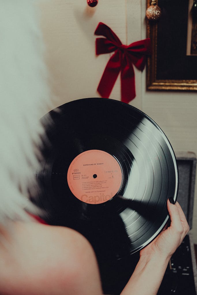 Hand holding a vinyl record with a festive Christmas background featuring a red ribbon and decorations.