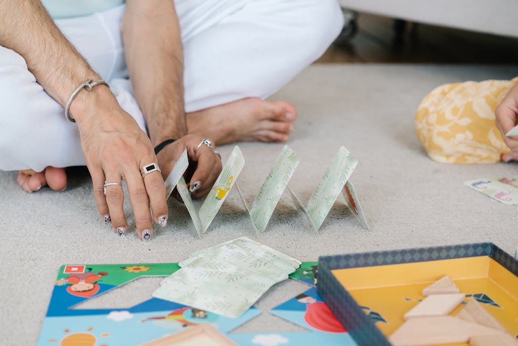Hands building a card house on a carpet, capturing a playful and intimate moment indoors.