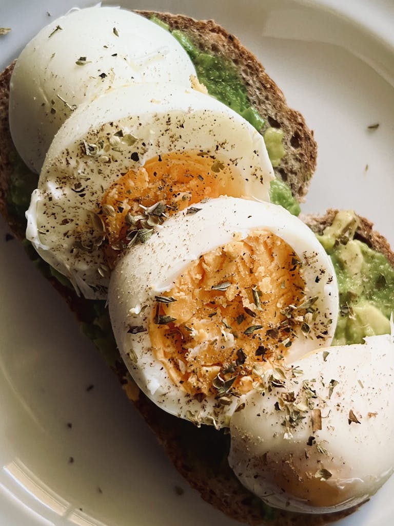 Healthy avocado toast topped with sliced boiled eggs and a sprinkle of herbs.