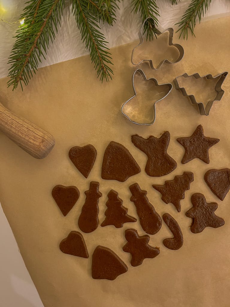 Holiday-themed cookie dough shapes with cutters on parchment paper, ready for baking.
