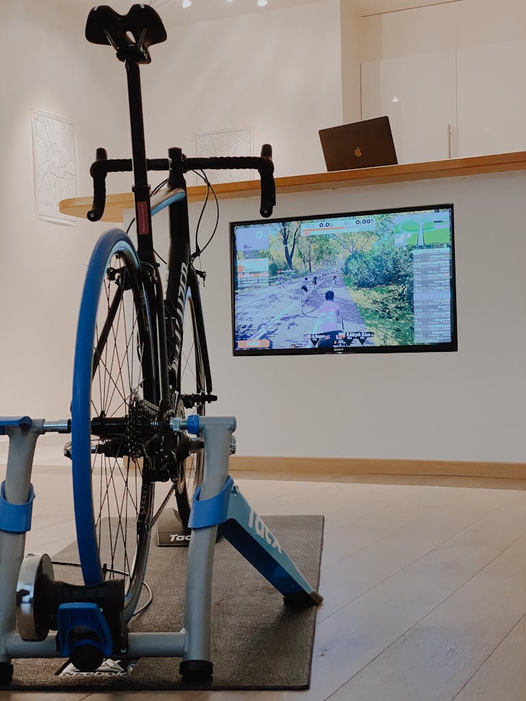 Home cycling setup showing a bike on a trainer with a virtual cycling app on screen.