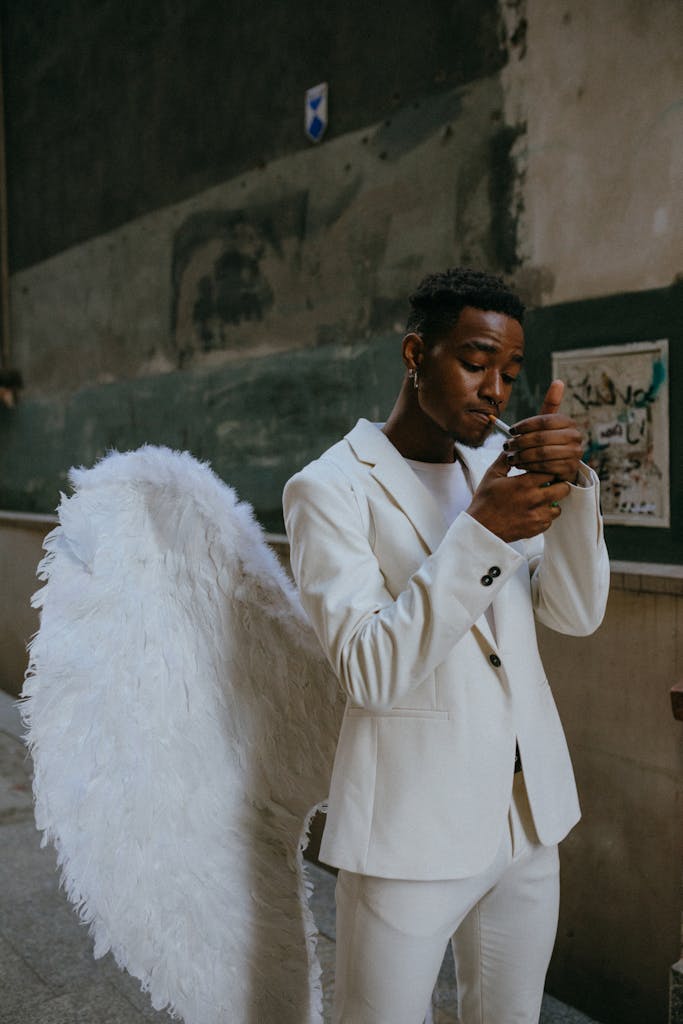 Man in white angel costume lighting a cigarette in an urban setting.
