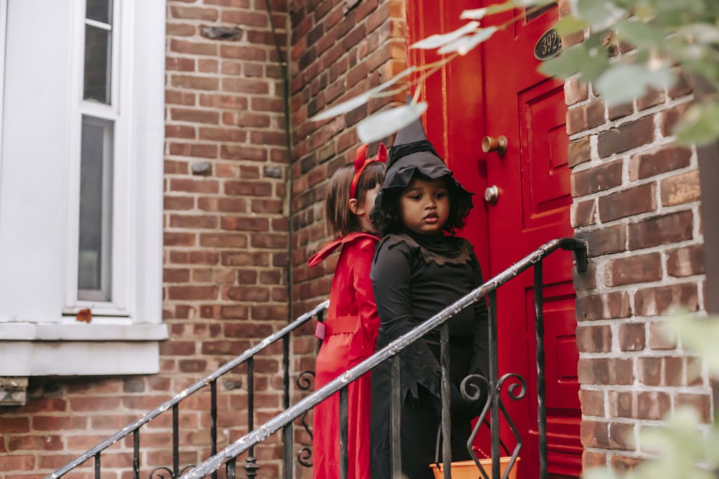 Multiethnic kids dressed for Halloween celebrations standing near front door of red brick house playing trick or treat custom