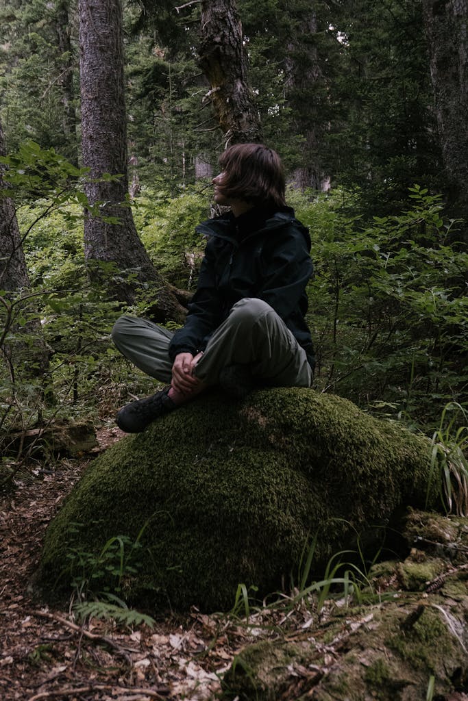 Person sitting on a moss-covered rock in a serene, lush forest setting.