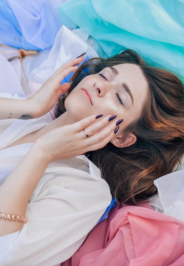 Relaxed young woman with closed eyes surrounded by colorful fabric, exuding calm and tranquility.