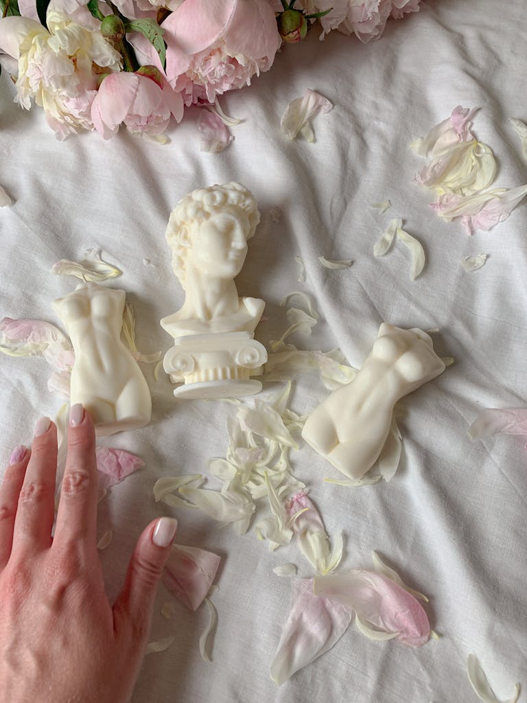 Sculptural soaps arranged on rose petals with a woman's hand touching for decorative effect.