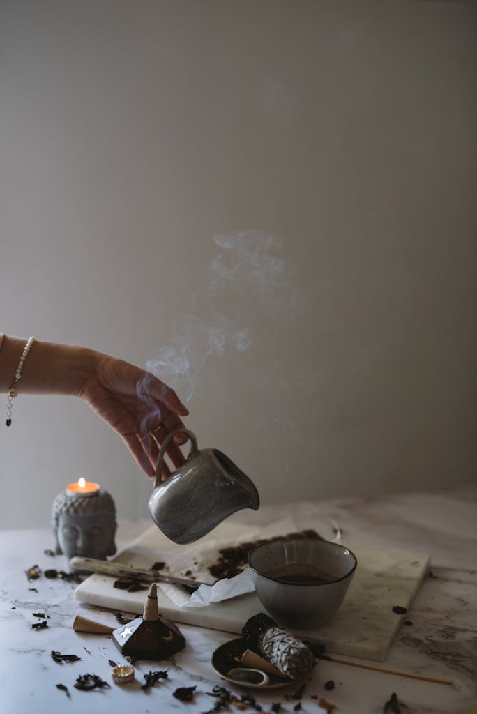 Serene indoor setting with hand pouring coffee, incense releasing smoke, and lit candle.