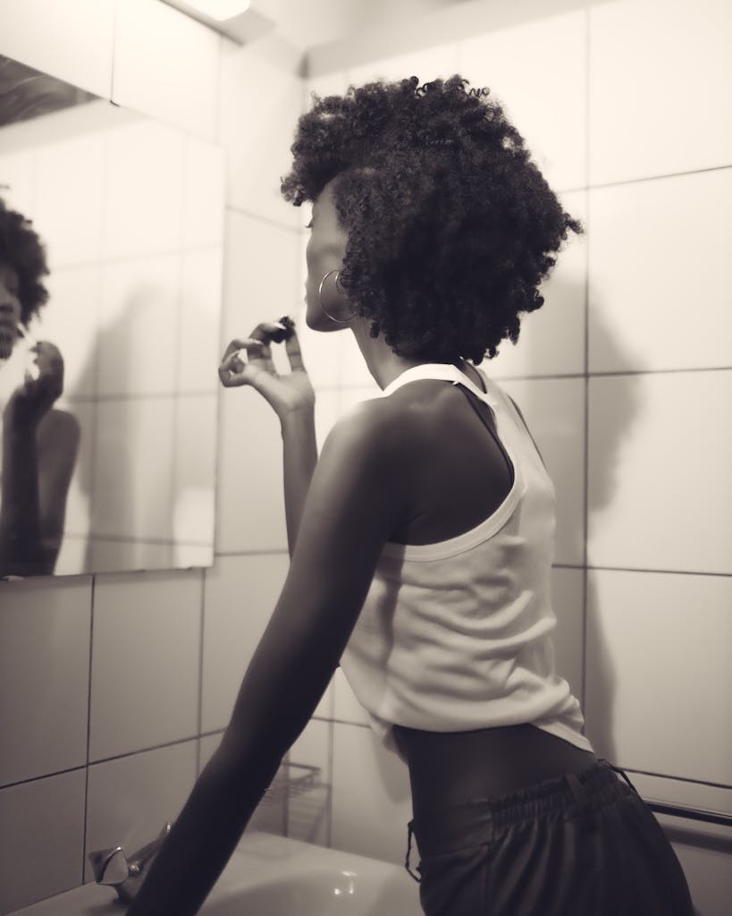Stylish woman applying lipstick in a modern tile-covered bathroom.
