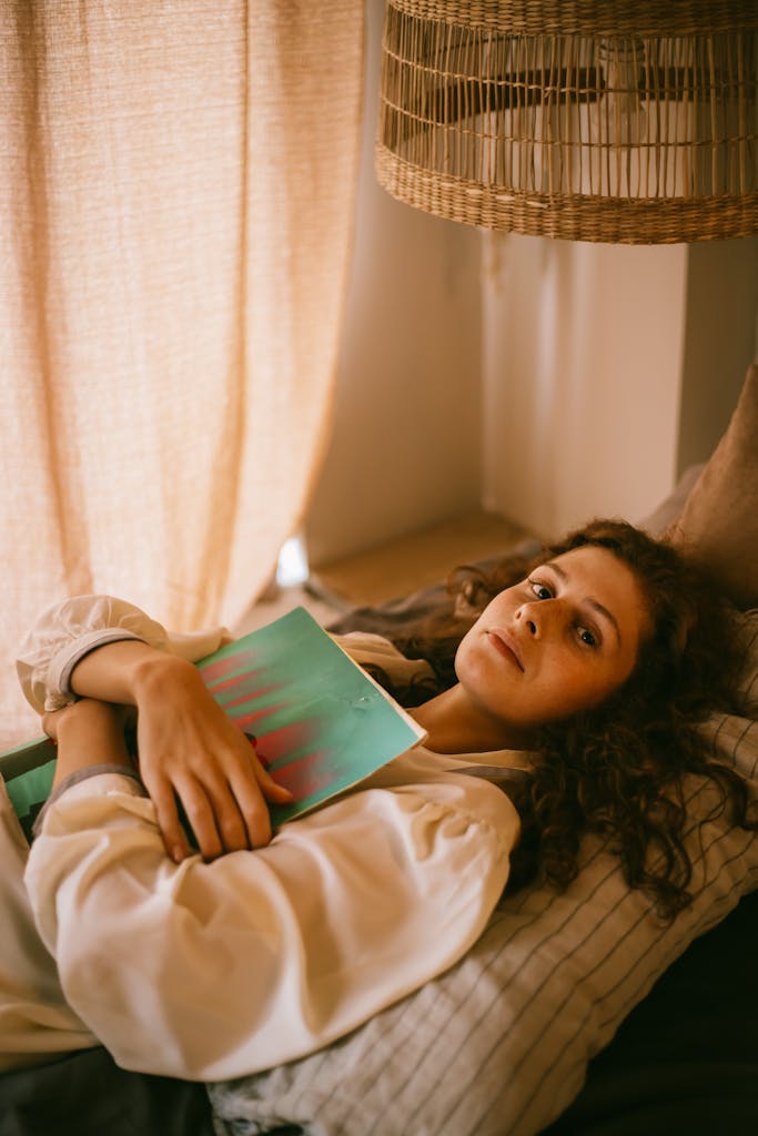 Teenager lying in bed with a book in a warm, cozy bedroom setting.