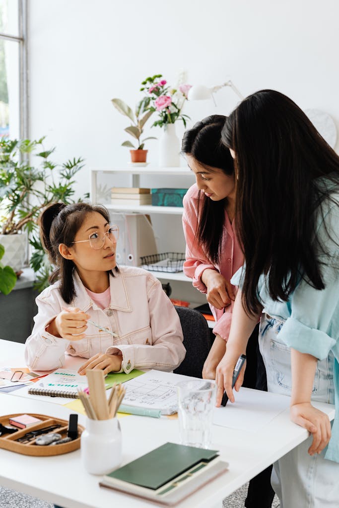 Three Asian women engaged in a collaborative discussion at a stylish office desk.