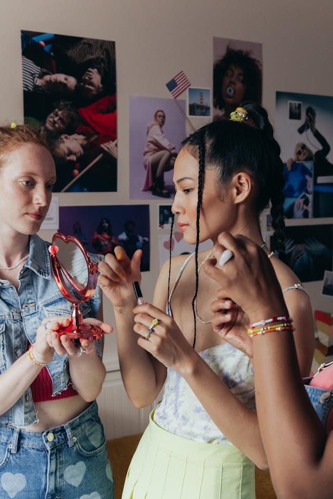 Three young women applying makeup together in a stylish, artistic room, focusing on beauty and fashion.