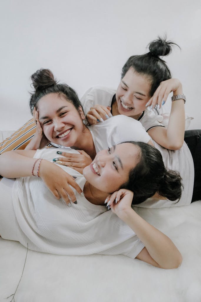Three young women laughing and embracing each other indoors, showcasing friendship and happiness.