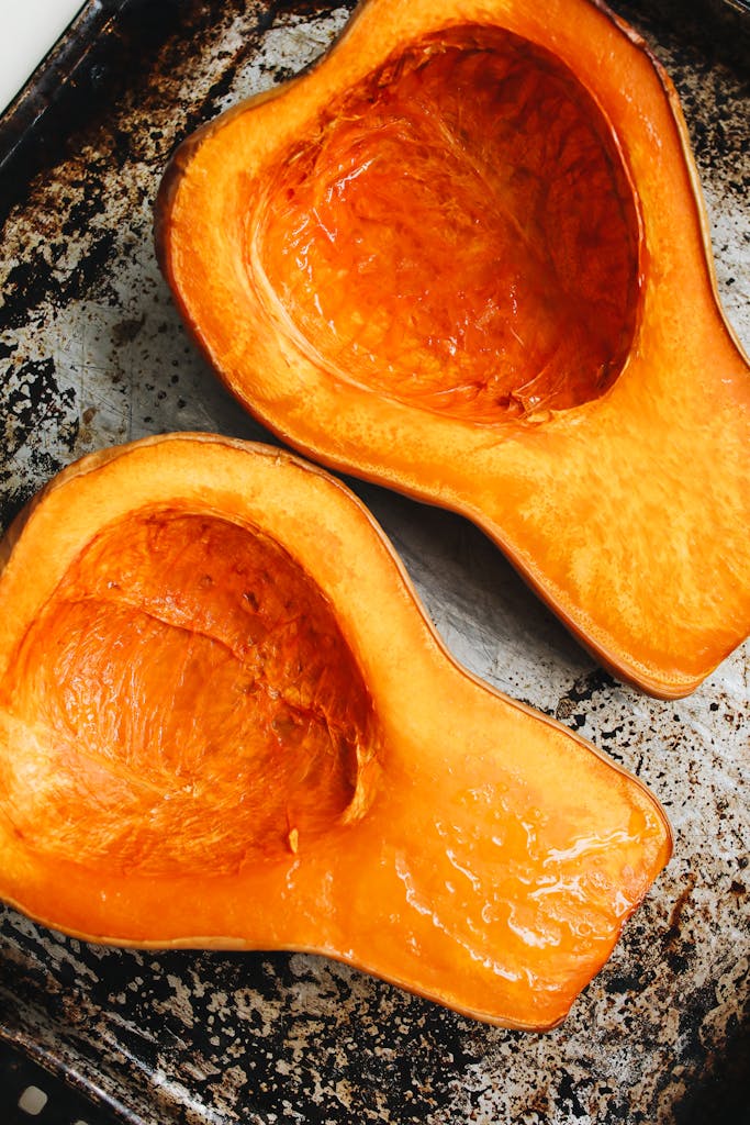 Top view of roasted butternut squash halves on a rustic metal baking tray.