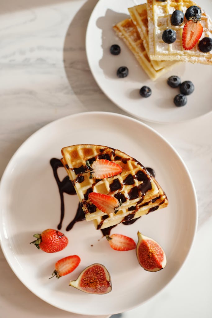 Top view of waffles with strawberries, figs, and chocolate syrup on plates.
