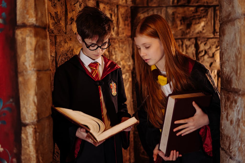 Two children in wizard costumes reading in a stone-walled corridor.