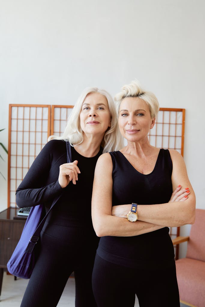 Two senior women in stylish activewear pose confidently indoors, exuding elegance and confidence.
