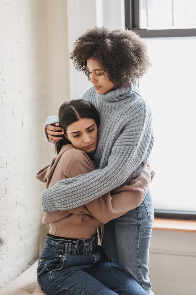Two women embrace warmly, offering emotional support in an indoor setting.