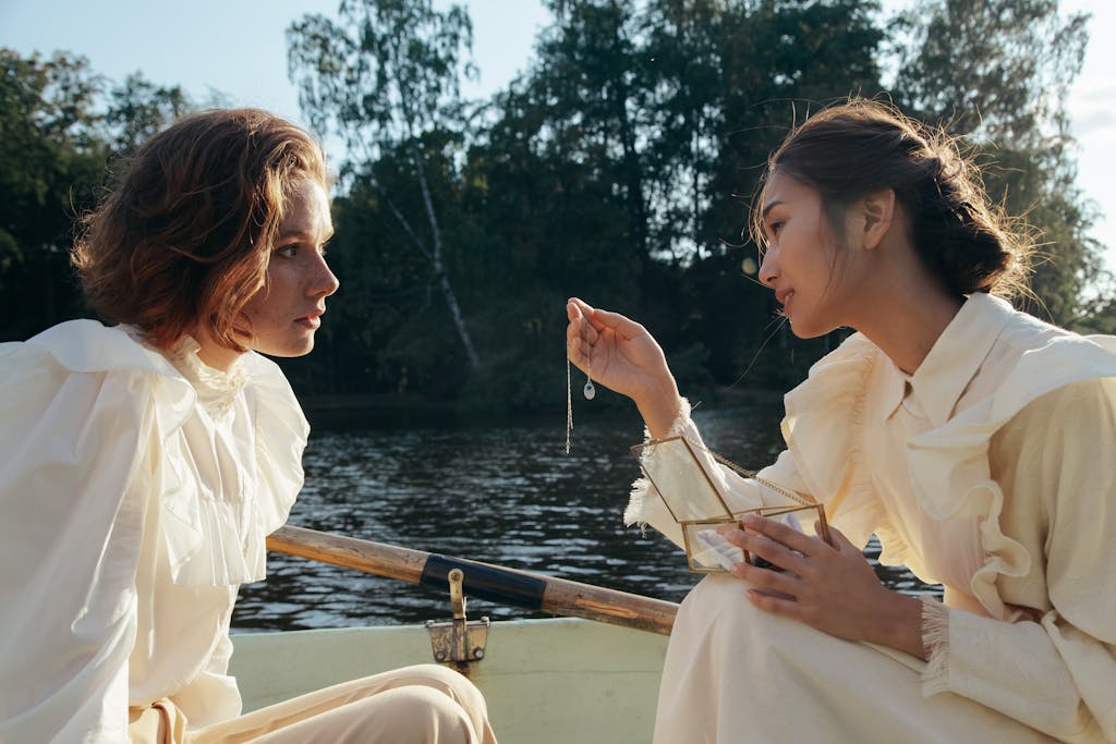 Two women in a boat share an intimate moment with a necklace under the sun.