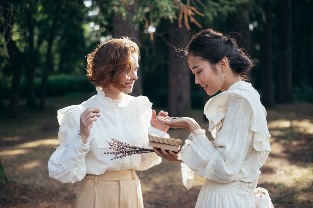Two women in vintage dresses sharing a moment with lavender in a sunlit forest.