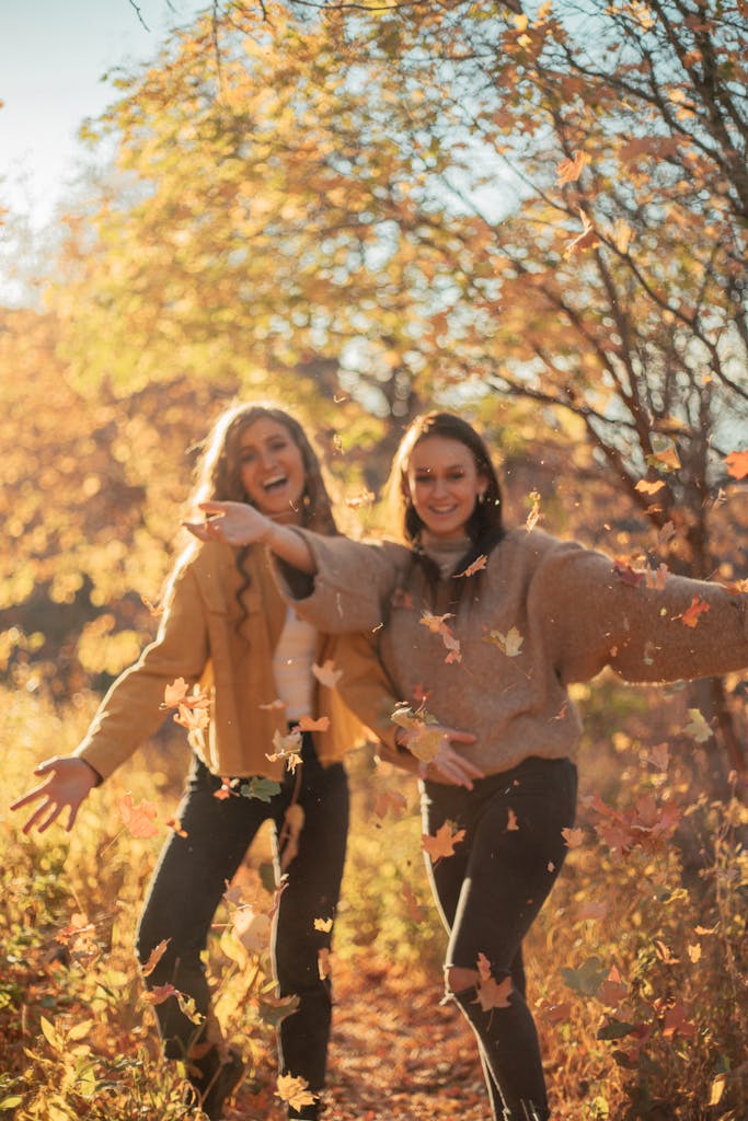 Two women joyfully play with autumn leaves, capturing the essence of a carefree fall day.
