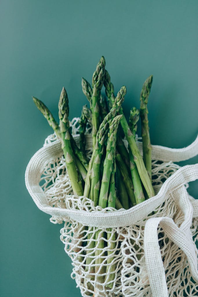 Vertical shot of fresh asparagus in a net bag against a green background, symbolizing healthy eating.