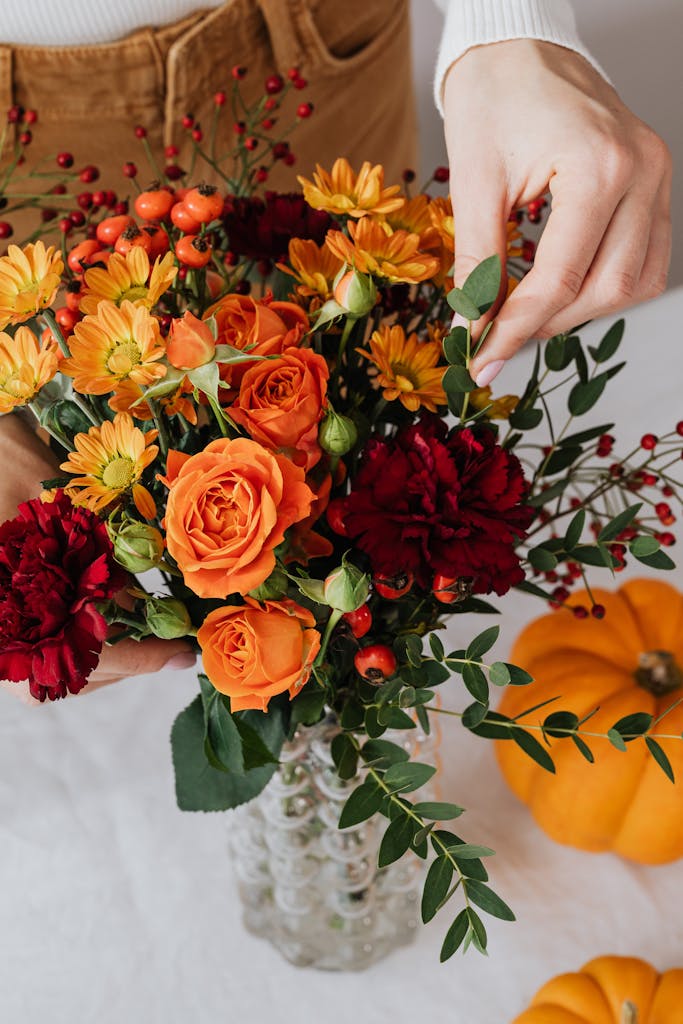 Vibrant autumn bouquet with oranges and reds in a glass vase, enhanced by seasonal decor.