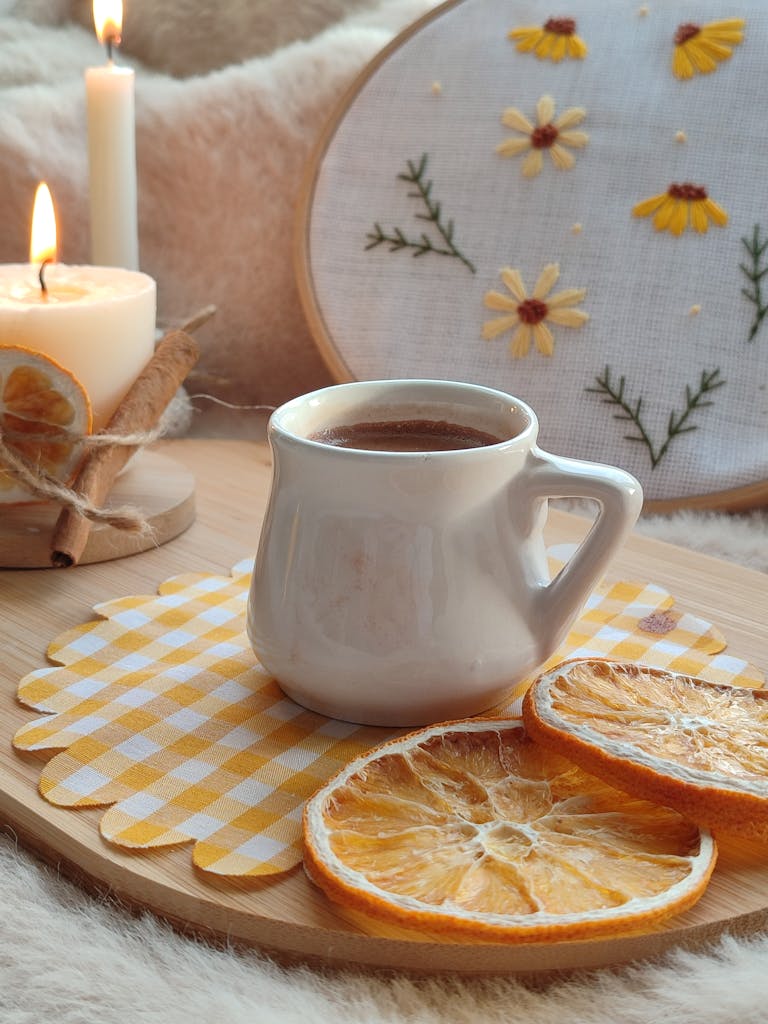 Warm and cozy autumn setup with a mug, candles, and dried oranges.