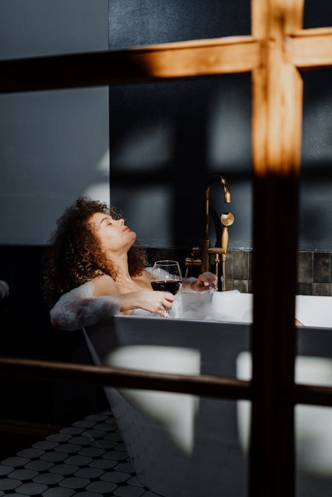 Woman enjoying a relaxing bath with foam and wine, embracing relaxation.