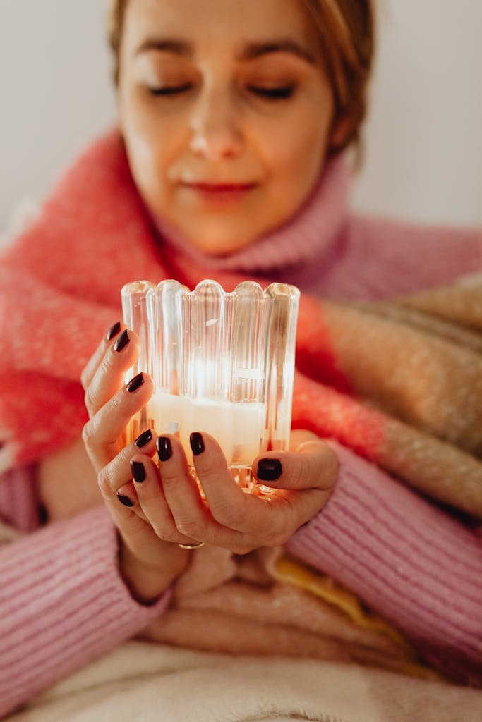 Woman holding a lit candle, wrapped in a scarf, enjoying a moment of relaxation indoors.