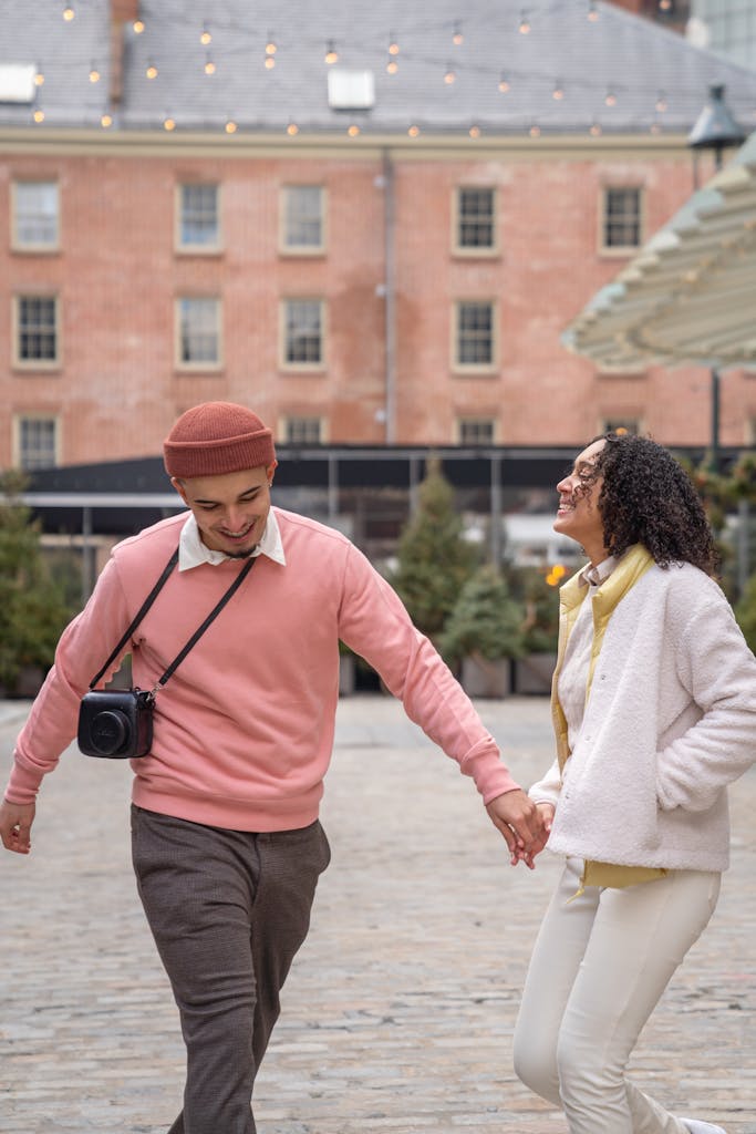 Young couple joyfully holding hands while walking in a city square.
