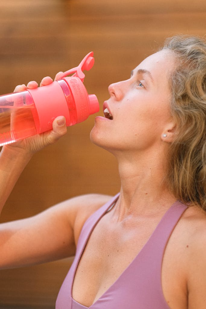 Young woman in activewear hydrating with a pink water bottle during an outdoor workout.